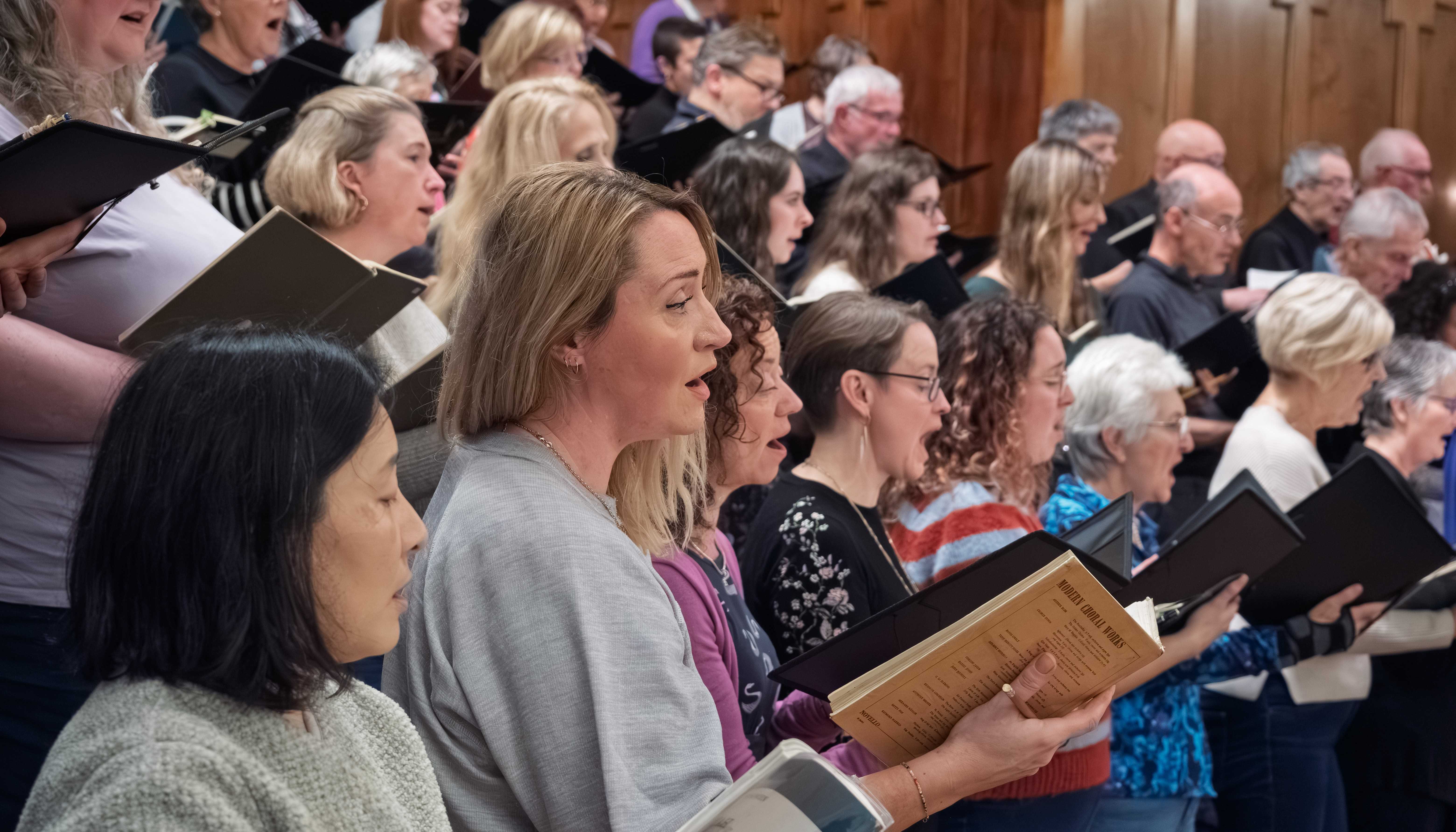 Part of the choir at a dress rehearsal in the Albert Hall, Nottingham.   The singers are dressed informally and are holding musical scores.