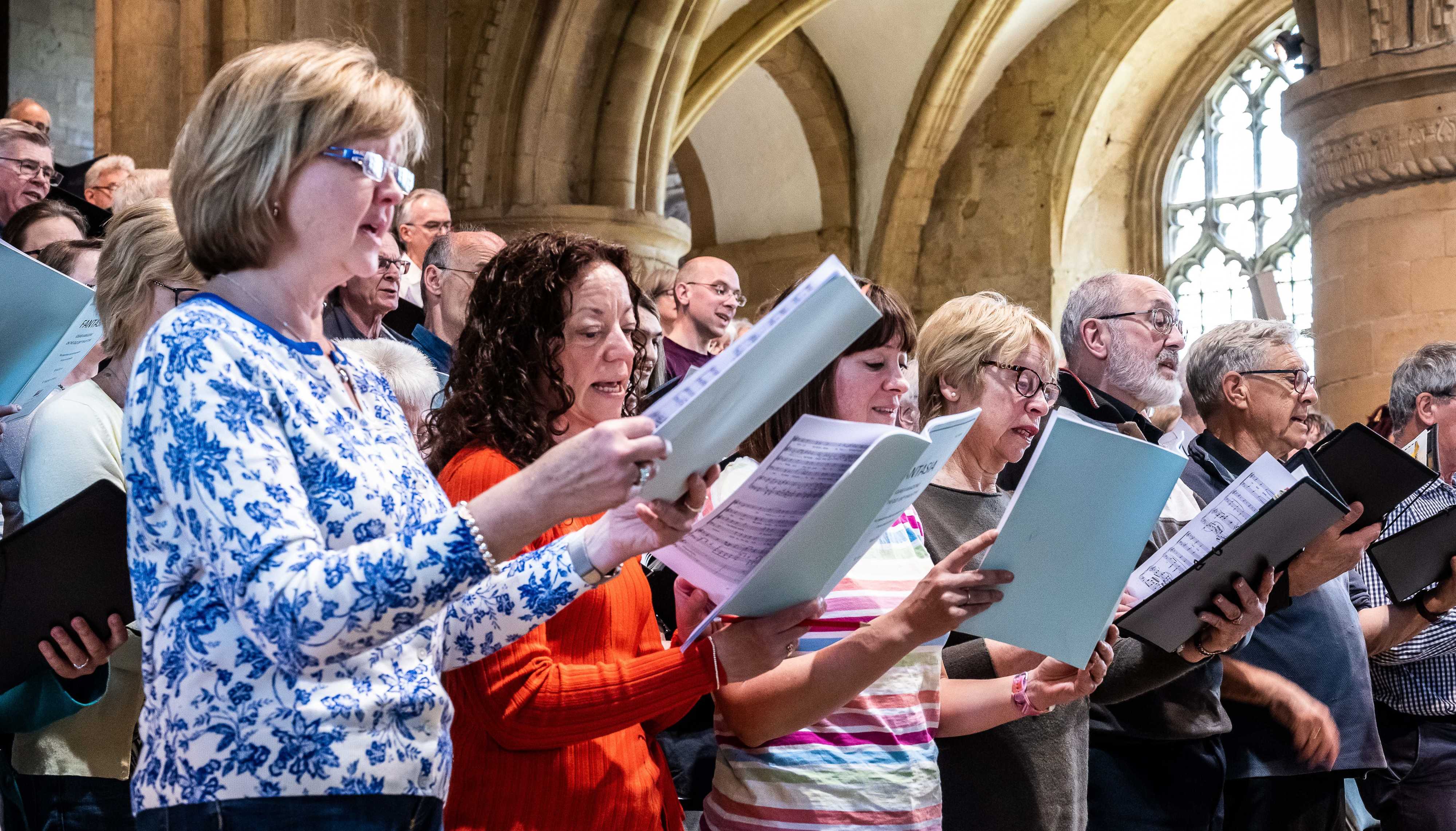 Close up of part of the choir during a dress rehearsal at Southwell Minster.  They are all holding music and singing and are dressed informally.