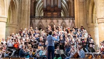 The choir singing at a dress rehearsal in Southwell Minster.  The choir is dressed informally, as are the conductor and orchestra.